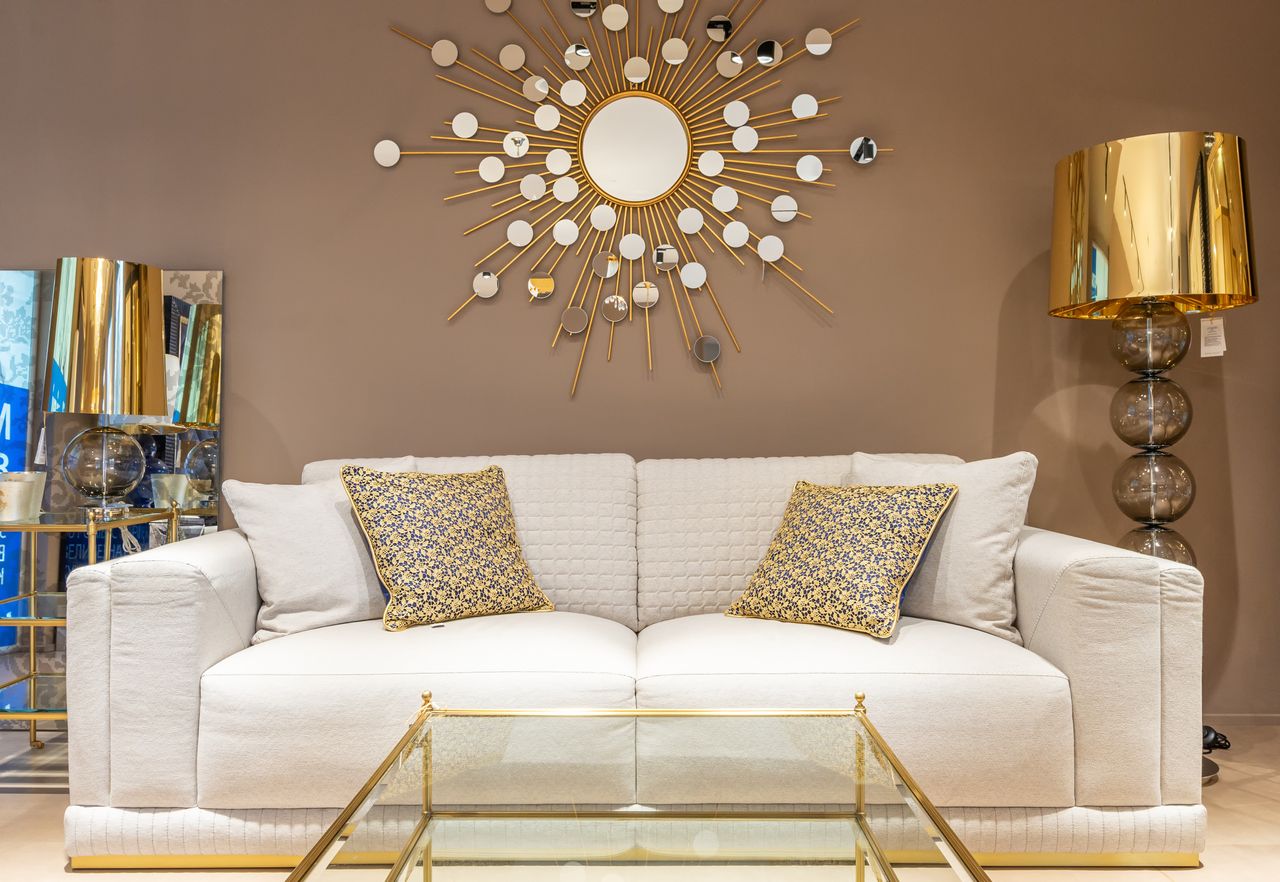 Comfortable white sofa with pillows placed near with floor lamp at wall with decorative elements in stylish living room of apartment